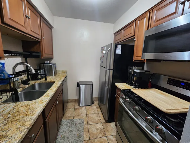 Kitchen with stainless steel appliances, light stone countertops, light tile patterned flooring, and wood finish cabinets