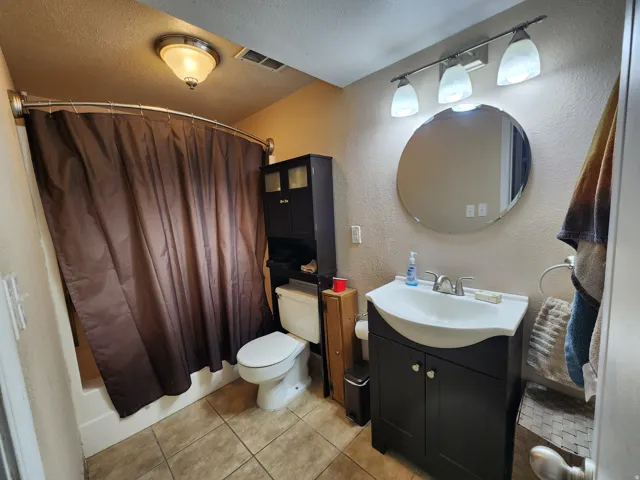 Bathroom featuring vanity, a textured wall, a textured ceiling, light tile patterned floors, and shower / bath combination with curtain