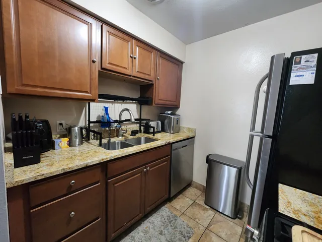 Kitchen with stainless steel appliances, light stone countertops, light tile patterned flooring, and wood finish cabinetry
