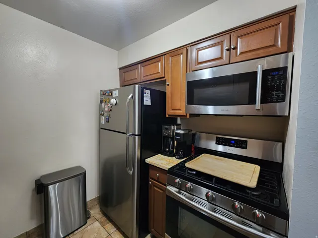 Kitchen with stainless steel appliances, light tile patterned flooring, wood finish cabinetry, and light stone countertops