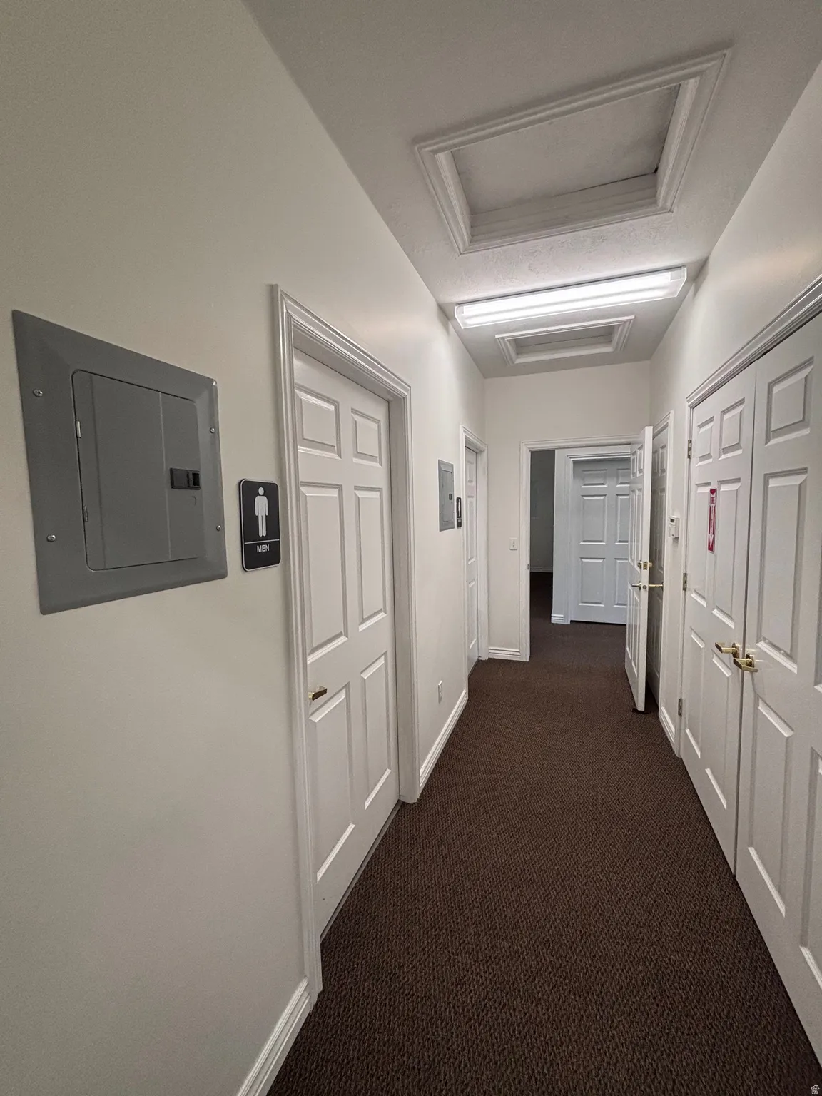 Hallway featuring electric panel and dark carpet
