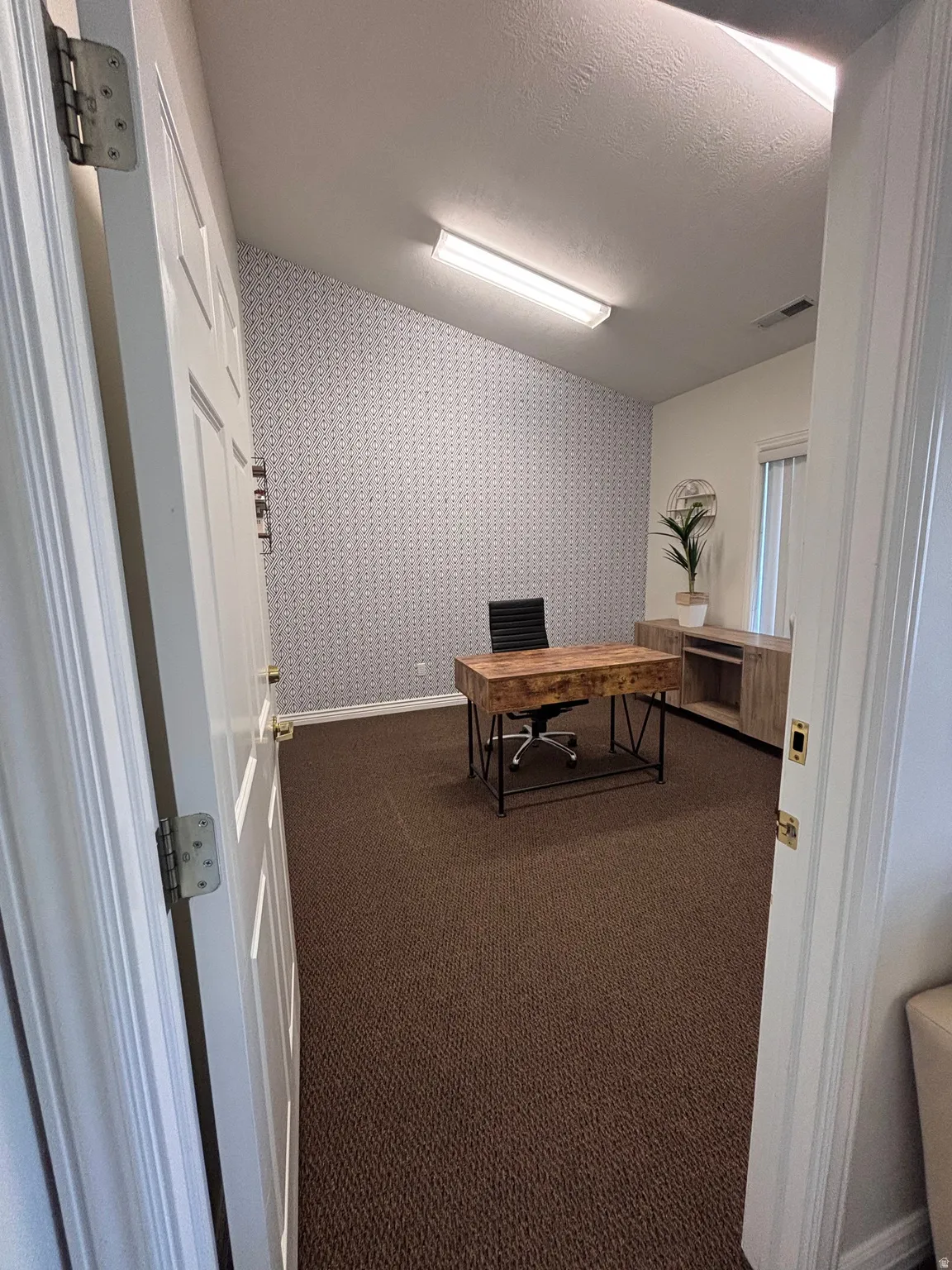 Office space featuring wallpapered walls, dark carpet, and a textured ceiling