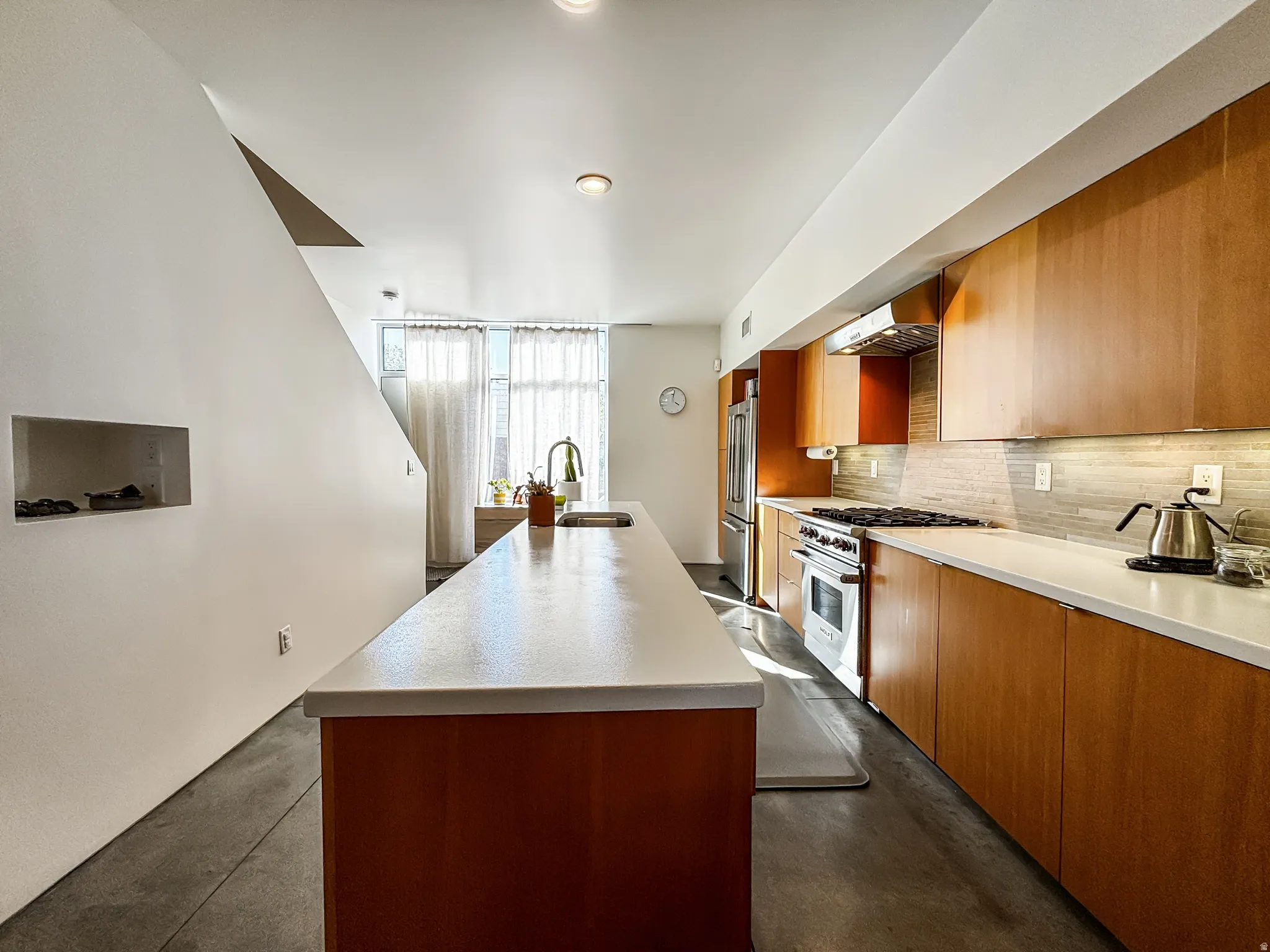 Kitchen featuring a kitchen island with sink, premium appliances, wood finish cabinetry, concrete floors, and extractor fan