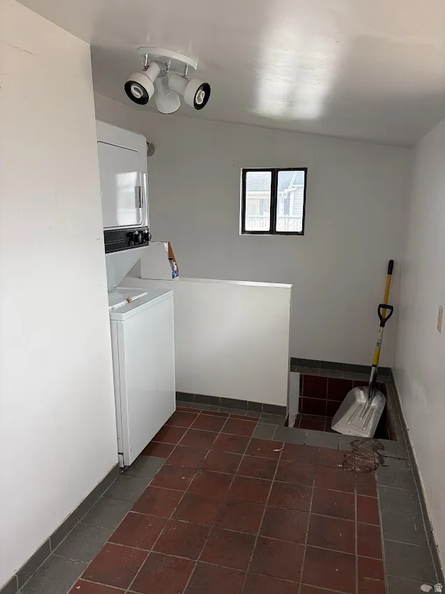 Laundry area with dark tile patterned floors and stacked washer / dryer