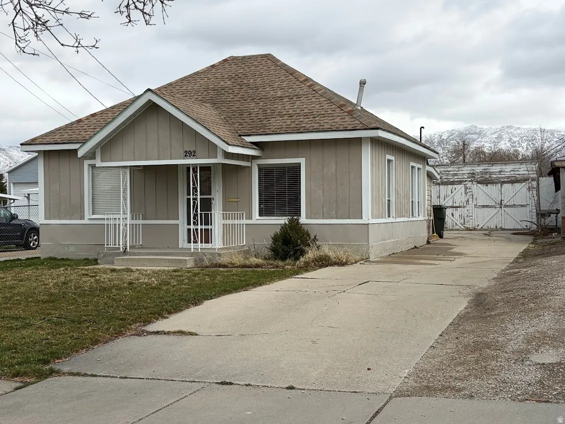 View of front of home with roof with shingles, a gate, board and batten siding, and driveway