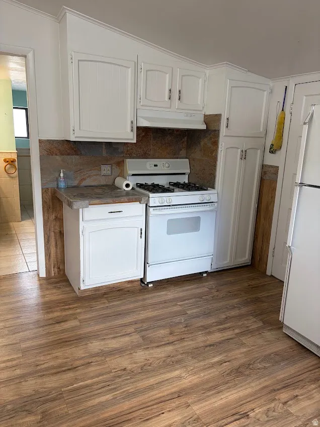 Kitchen with white appliances, white cabinets, a wainscoted wall, dark wood finished floors, and dark countertops