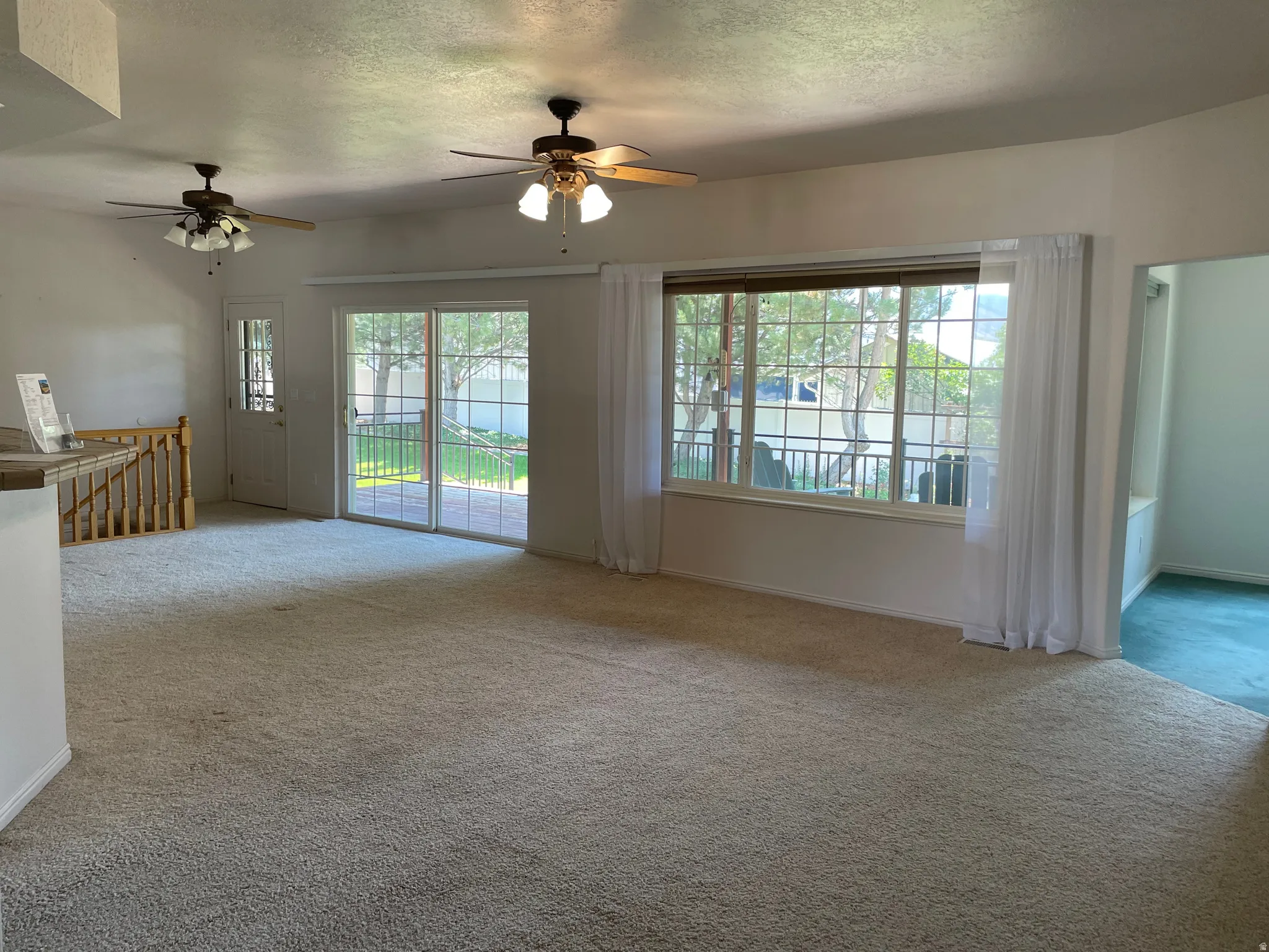 Open-concept living area featuring light-toned carpeting, two ceiling fans with integrated lighting, and a prominent picture window