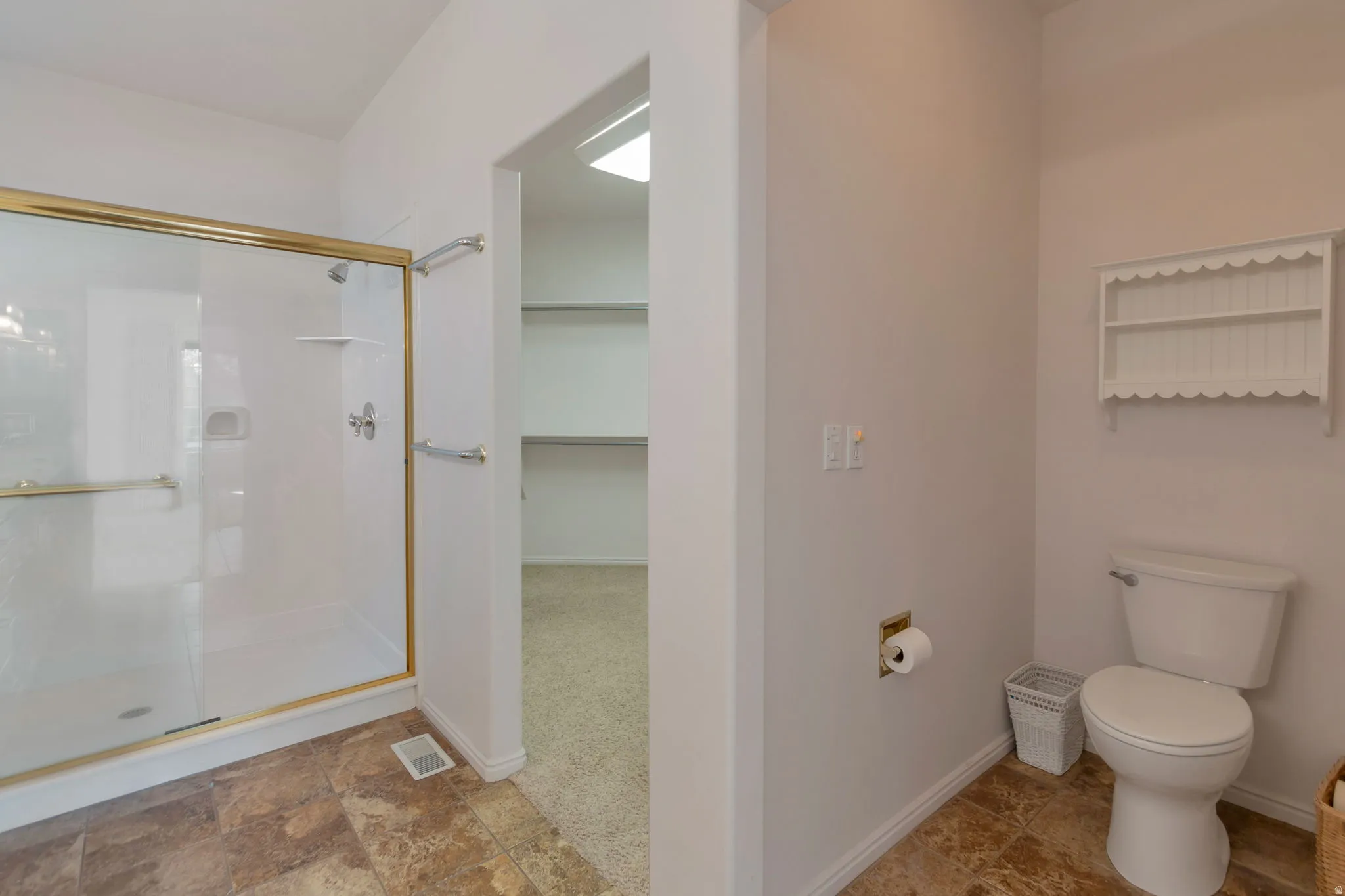 Full bath featuring a shower stall, stone finish floors, and a walk in closet