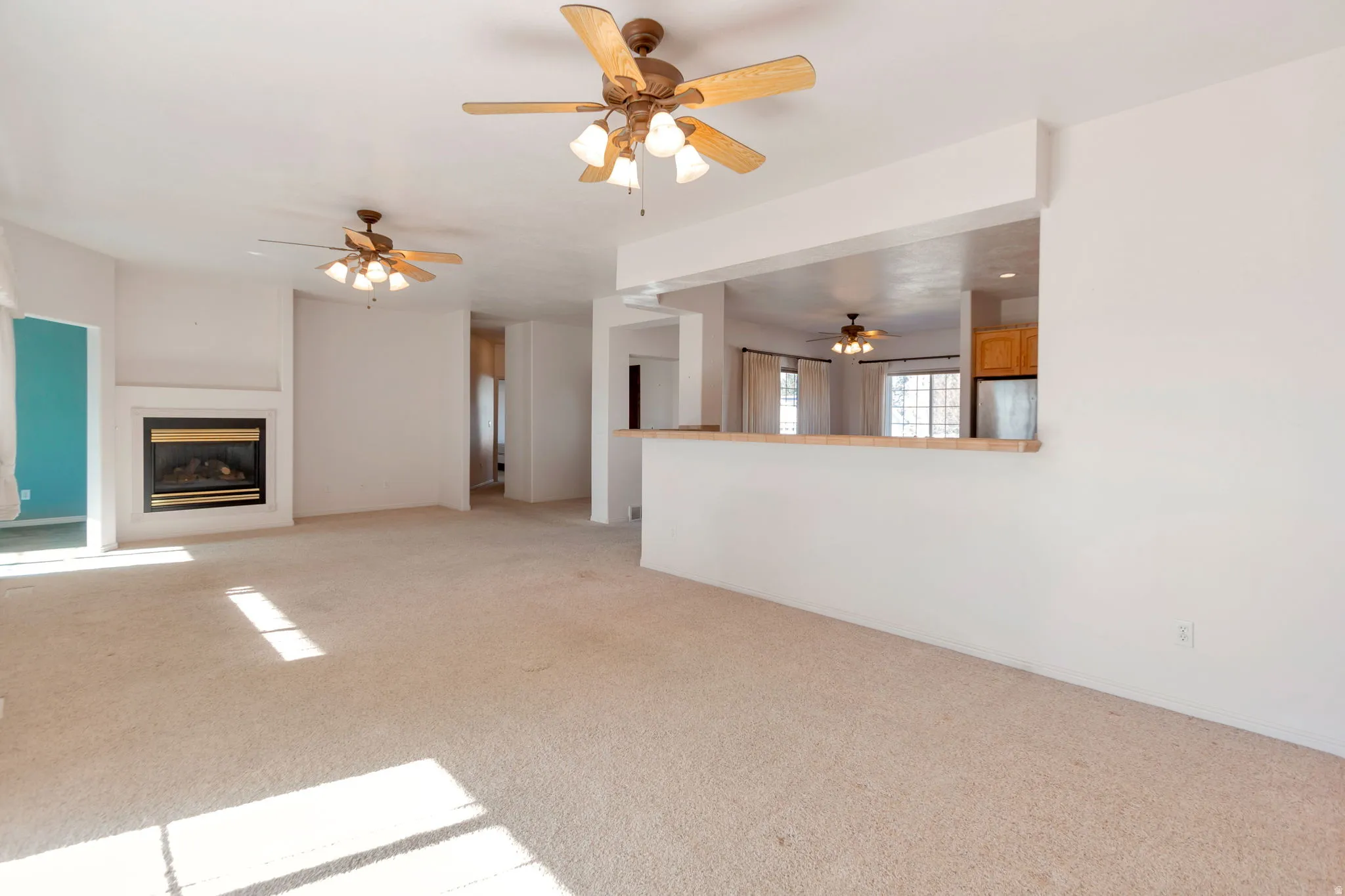 Unfurnished living room featuring light colored carpet, a glass covered fireplace, and a ceiling fan
