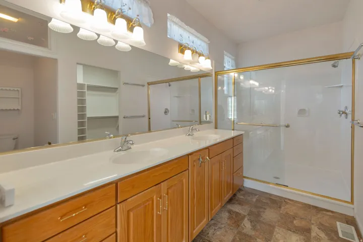 Bathroom with double vanity, stone finish floors, a shower stall, and a walk in closet
