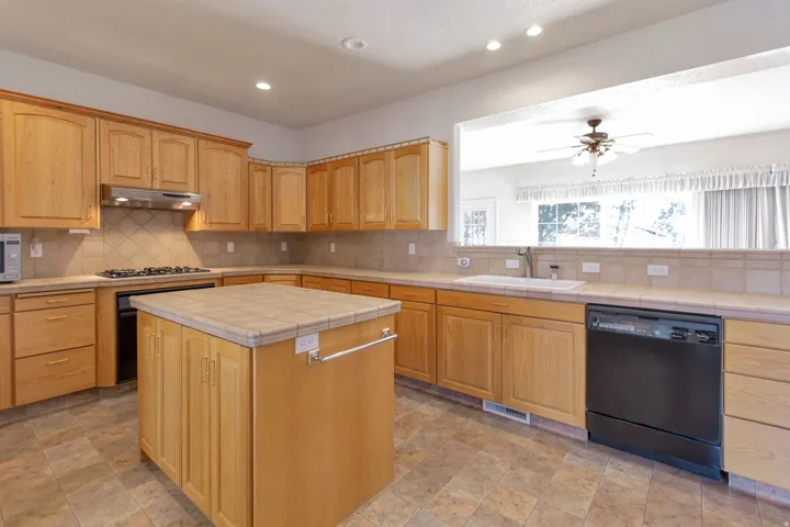 Kitchen with tile counters, dishwasher, ceiling fan, stone finish floors, and recessed lighting