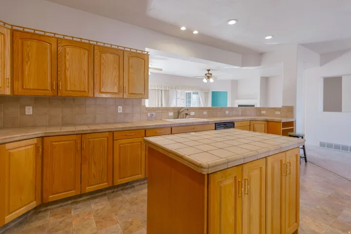 Kitchen featuring tile counters, a center island, ceiling fan, backsplash, and recessed lighting