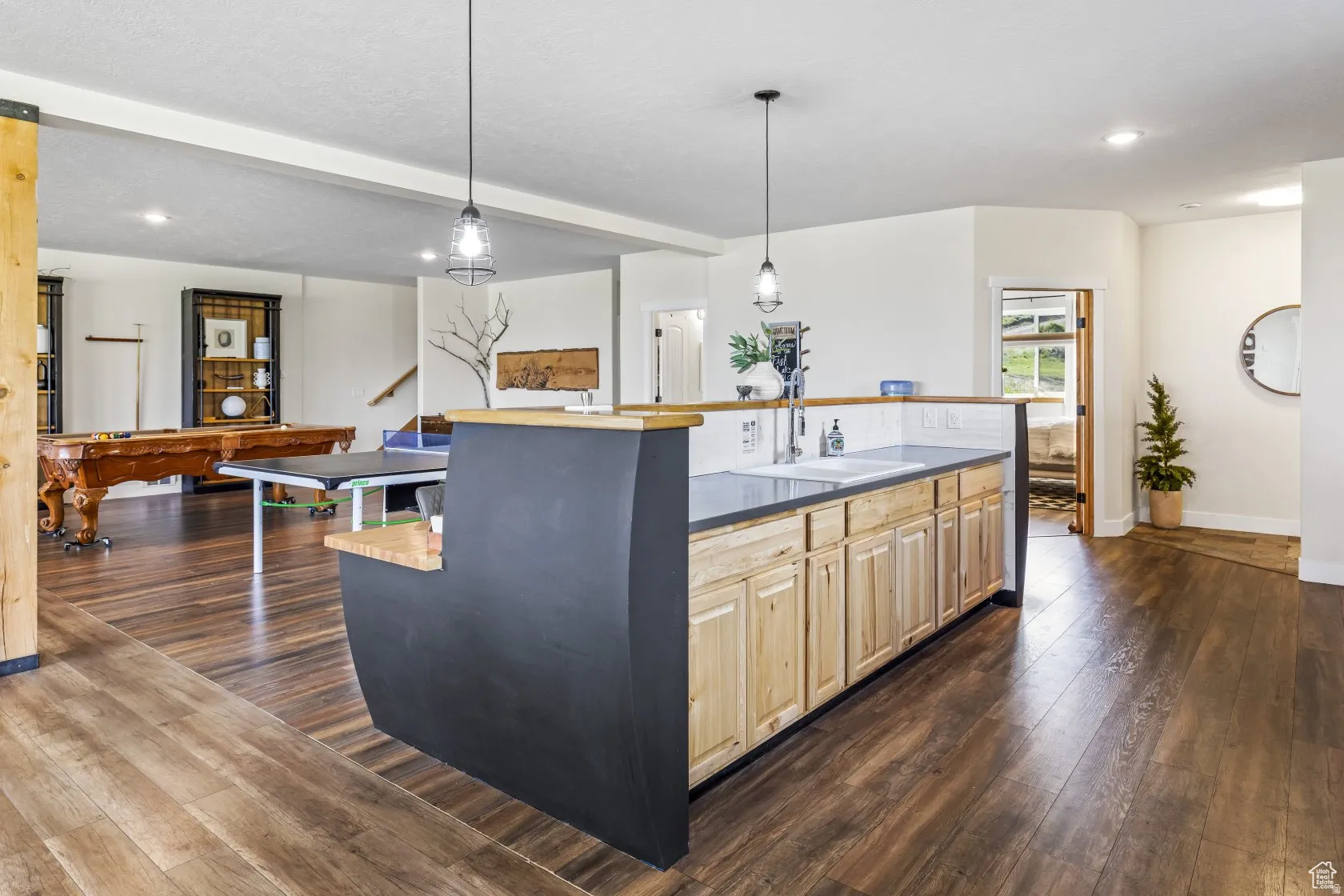 Kitchen featuring light wood finish cabinetry, dark wood-type flooring, decorative light fixtures, an island with sink, and beamed ceiling
