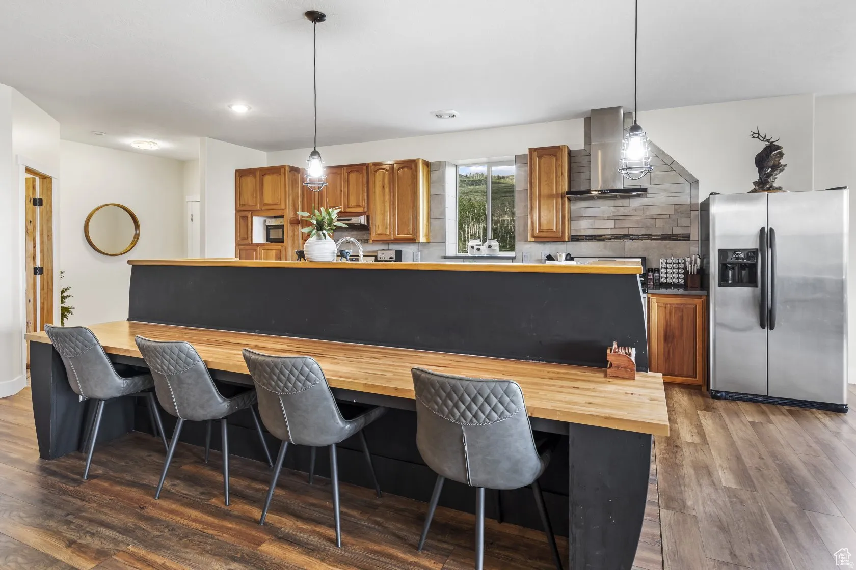 Kitchen featuring wood finish cabinetry, stainless steel appliances, tasteful backsplash, decorative light fixtures, and dark wood-type flooring