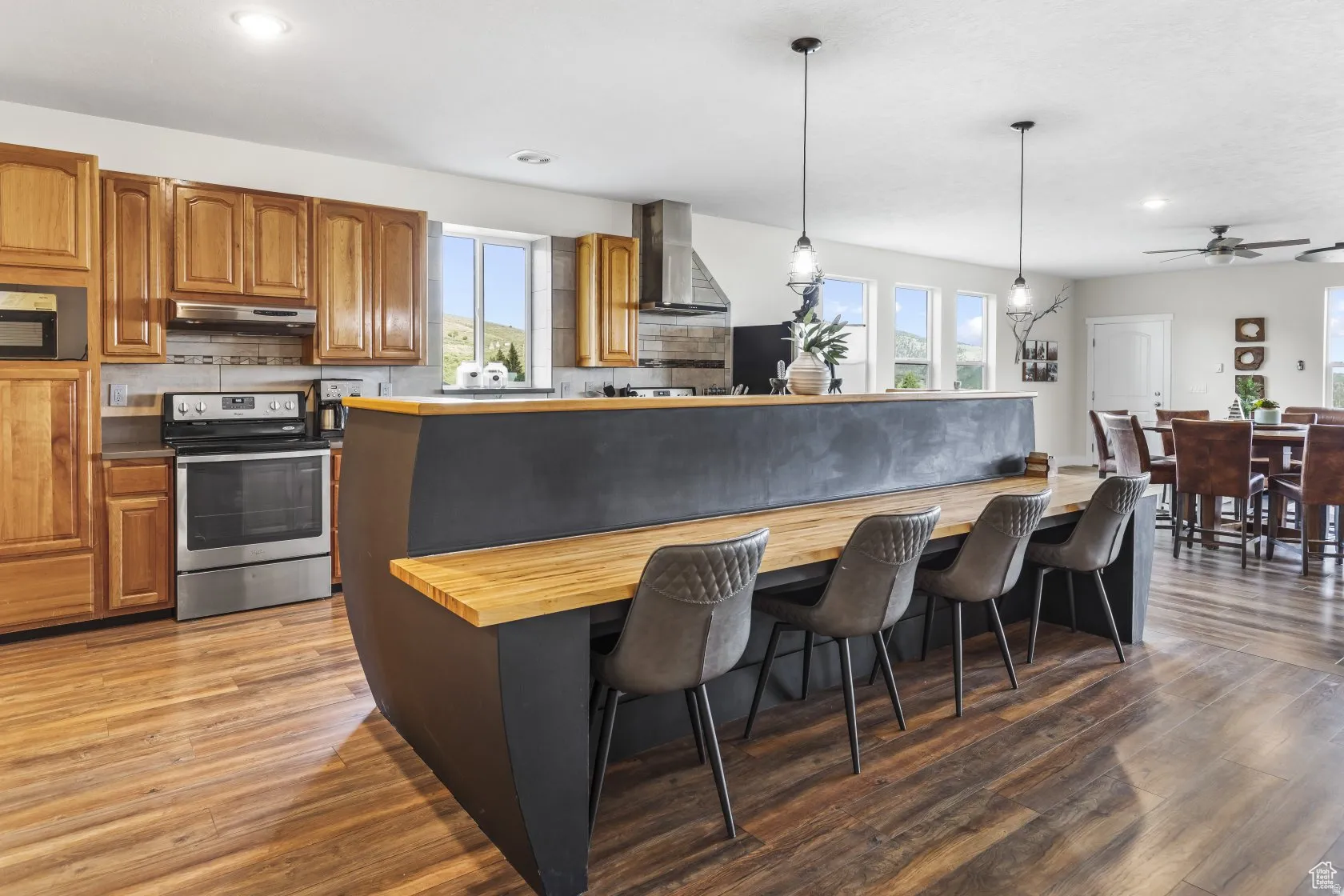 Kitchen featuring wood finish cabinetry, stainless steel electric range, a breakfast bar area, a center island, and pendant lighting