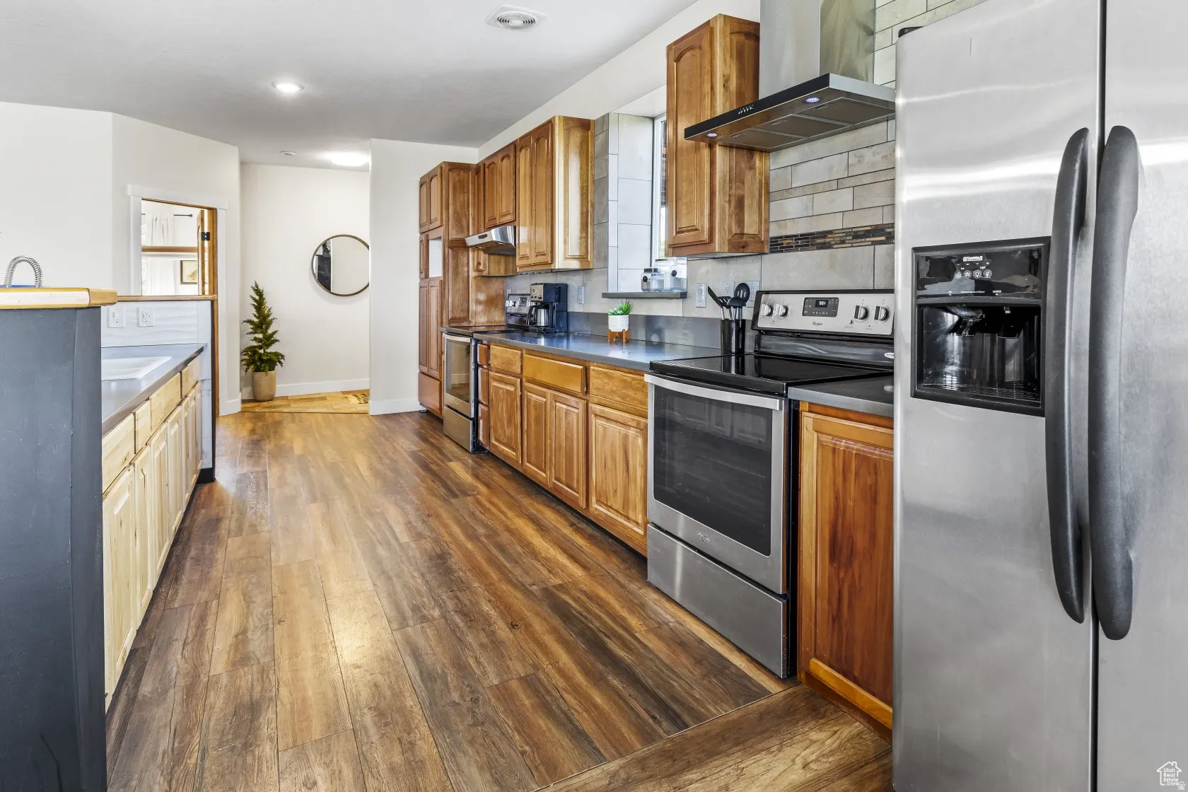 Kitchen featuring stainless steel appliances, dark wood-style floors, backsplash, wood finish cabinets, and dark countertops