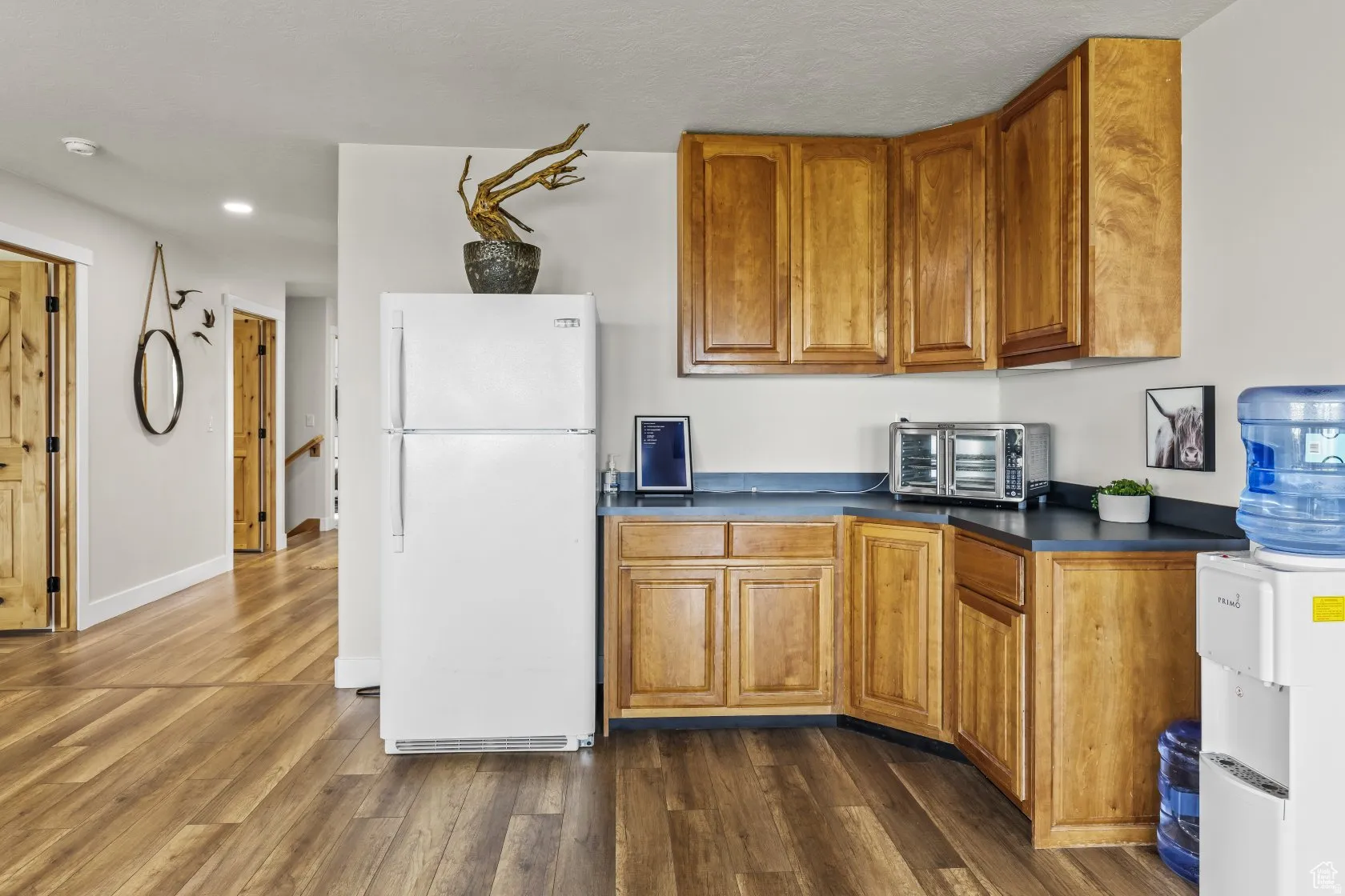 Kitchen featuring wood finish cabinetry, freestanding refrigerator, dark countertops, and dark wood finished floors