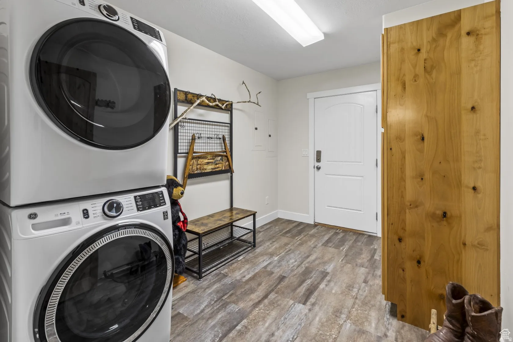 Laundry area with light wood-style flooring, stacked washer / drying machine, and electric panel