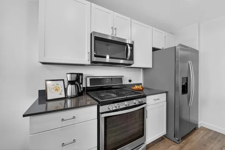 Kitchen with stainless steel appliances, white cabinets, wood finished floors, and dark stone countertops