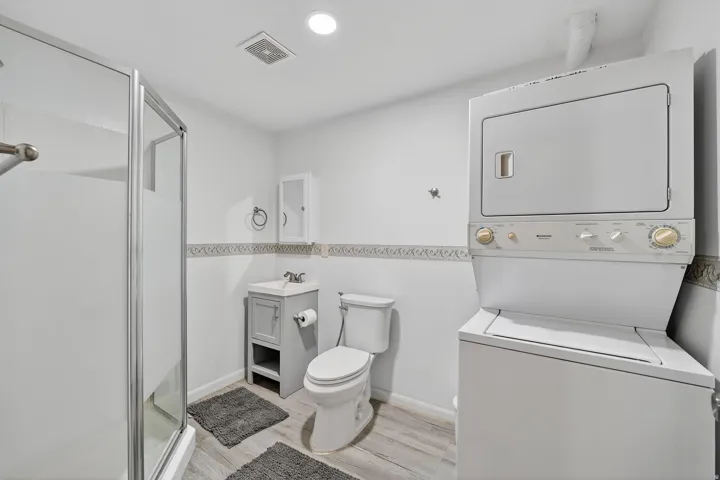 Bathroom featuring vanity, a shower stall, light wood finished floors, stacked washer / drying machine, and recessed lighting