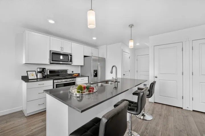 Kitchen with stainless steel appliances, white cabinetry, light wood-style floors, and an island with sink