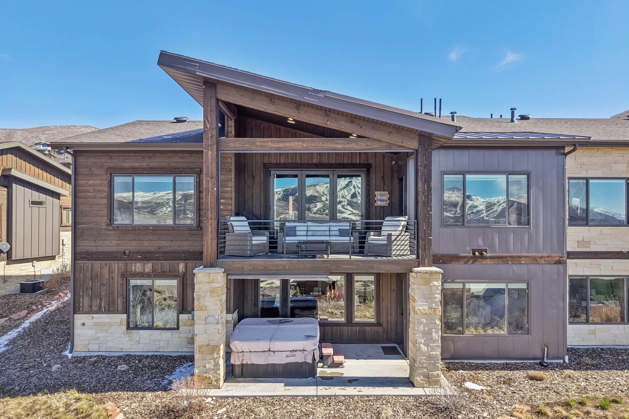 Back of property featuring a patio, a balcony, a shingled roof, and stone siding