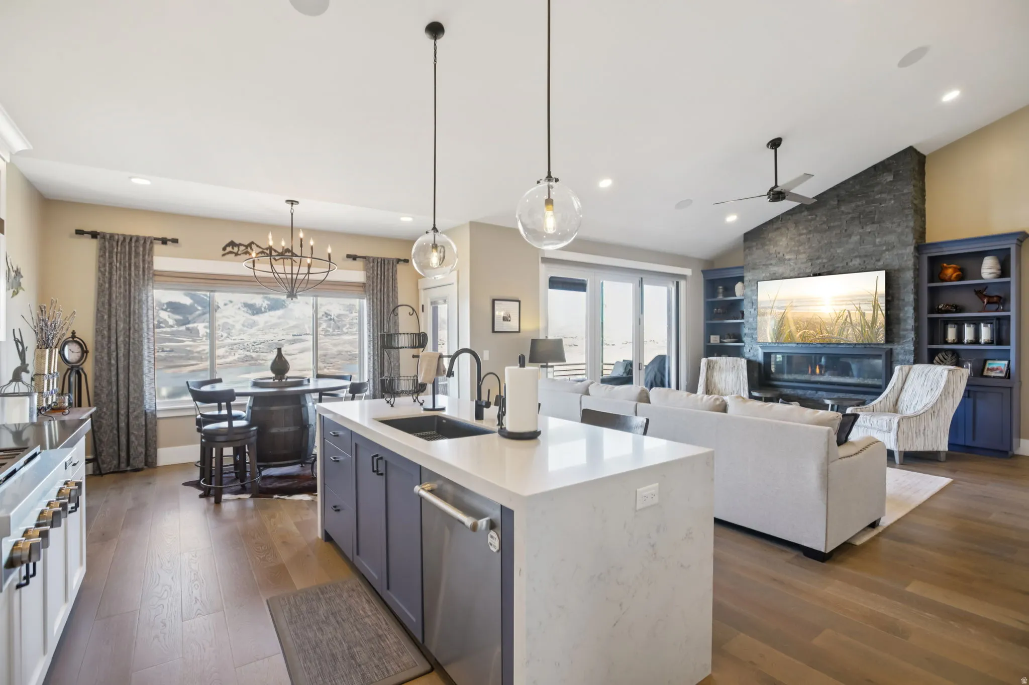 Kitchen featuring light wood-style floors, an island with sink, open floor plan, light stone counters, and lofted ceiling