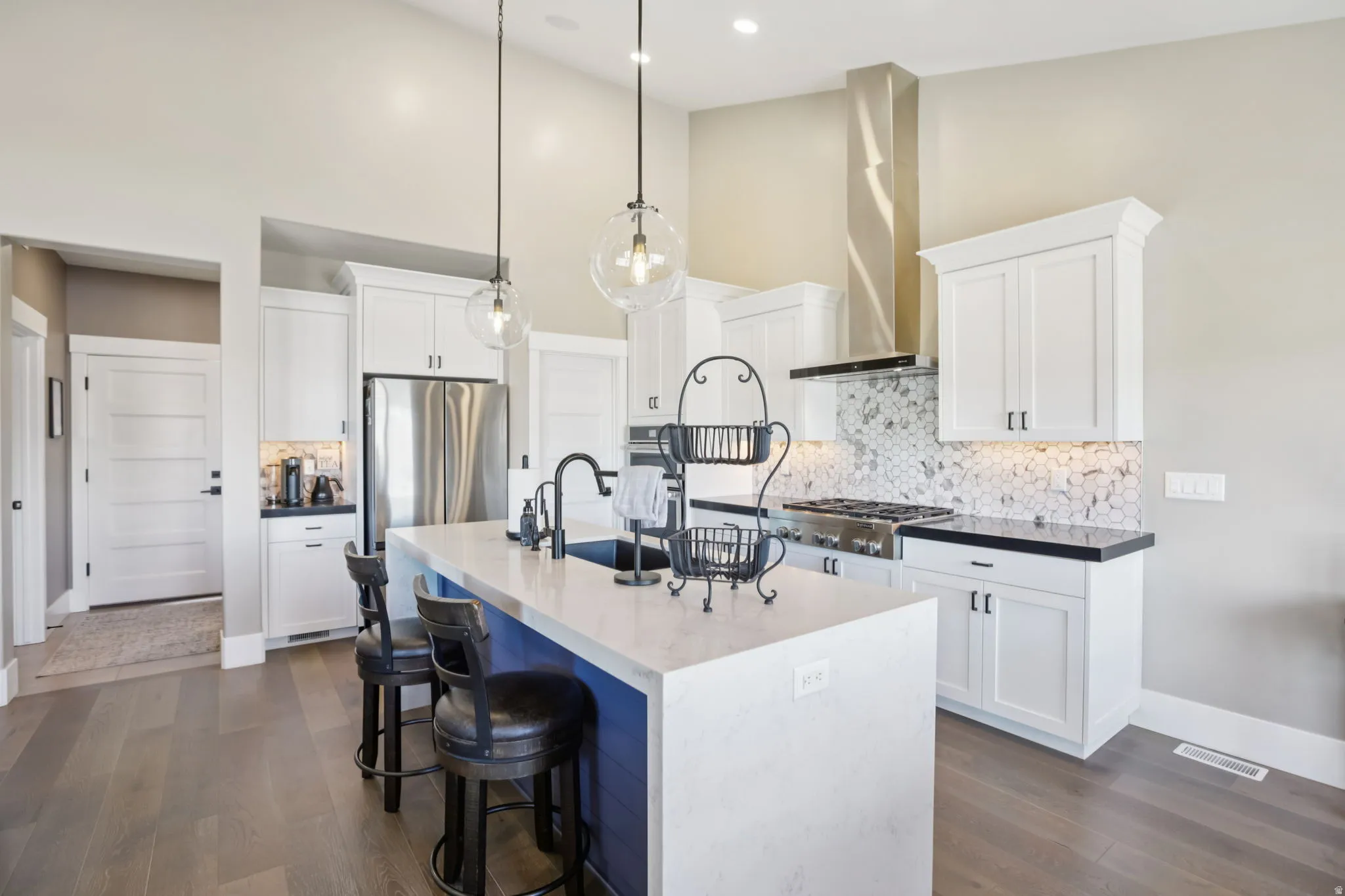 Kitchen with backsplash, a kitchen bar, white cabinets, a center island with sink, and a high ceiling