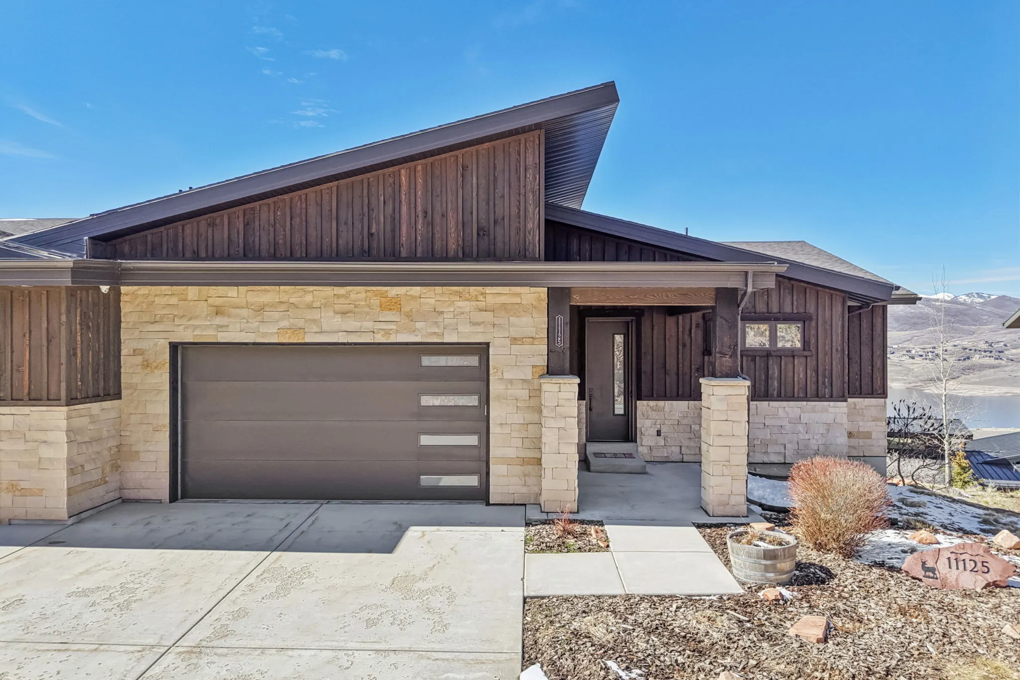 Contemporary house featuring stone siding, a garage, concrete driveway, and board and batten siding