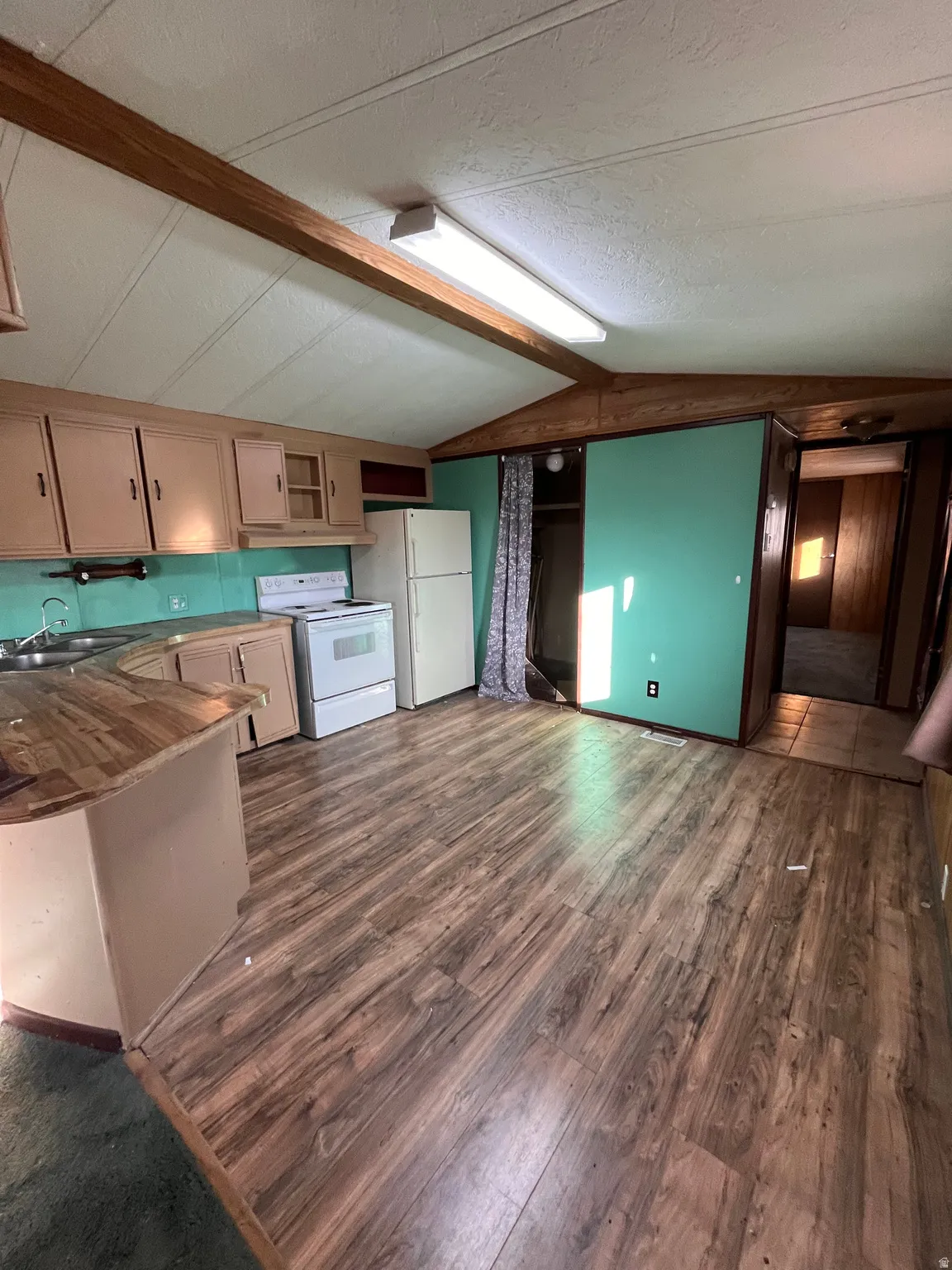 Kitchen featuring white appliances, dark wood finished floors, a textured ceiling, a peninsula, and beam ceiling
