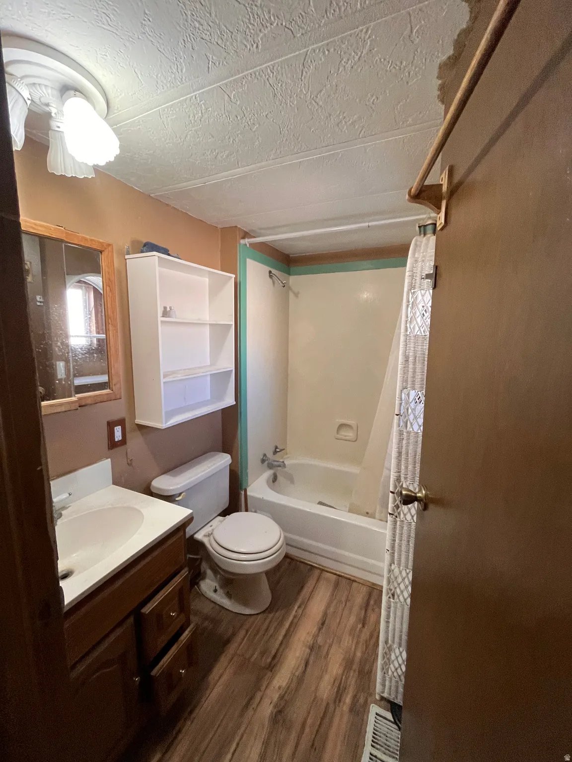 Bathroom with vanity, shower / bath combo with shower curtain, dark wood-type flooring, and a textured ceiling