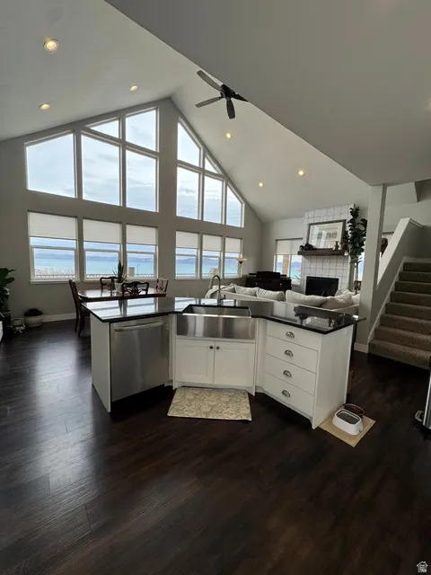 Kitchen with open floor plan, a high ceiling, white cabinetry, dark wood-style flooring, and stainless steel dishwasher