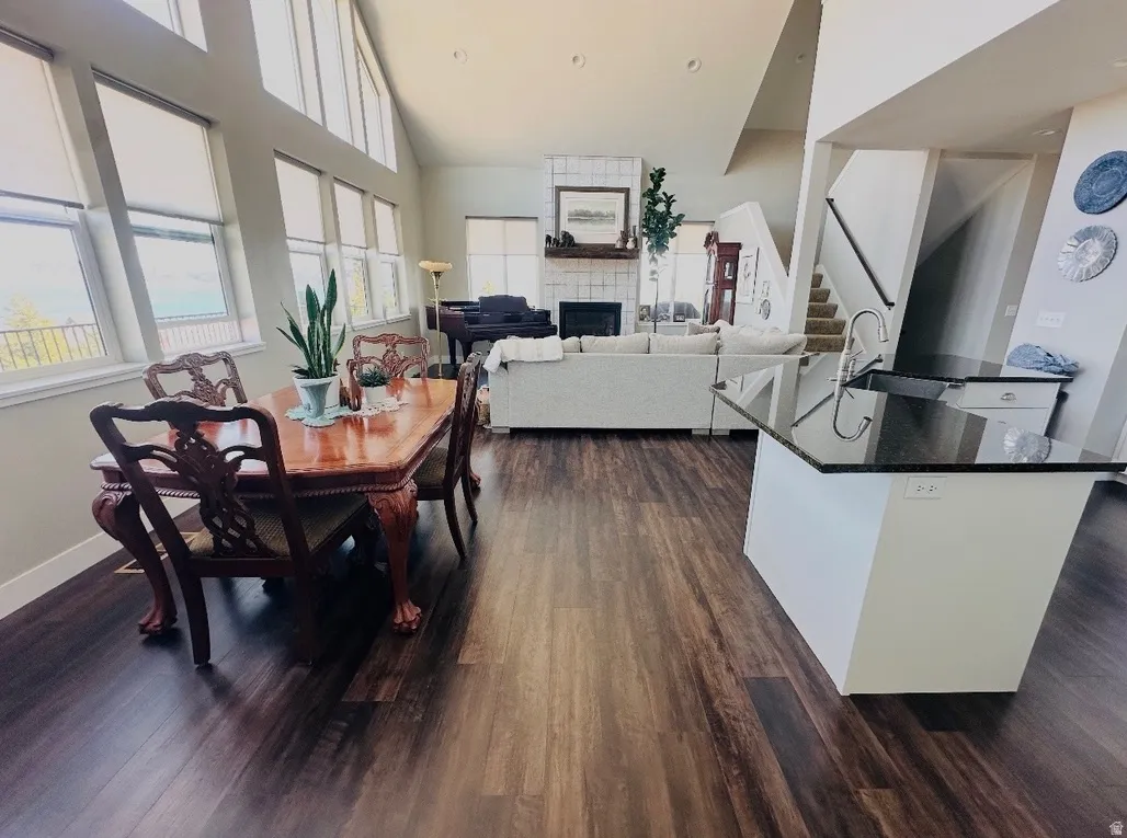Dining space with a tile fireplace, dark wood-type flooring, and a high ceiling