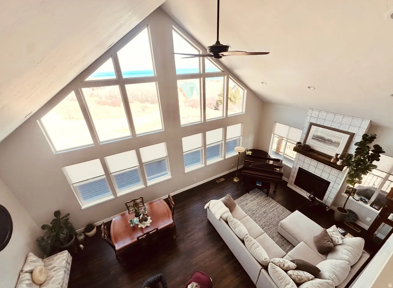 Living area with ceiling fan, a tiled fireplace, dark wood finished floors, and a high ceiling