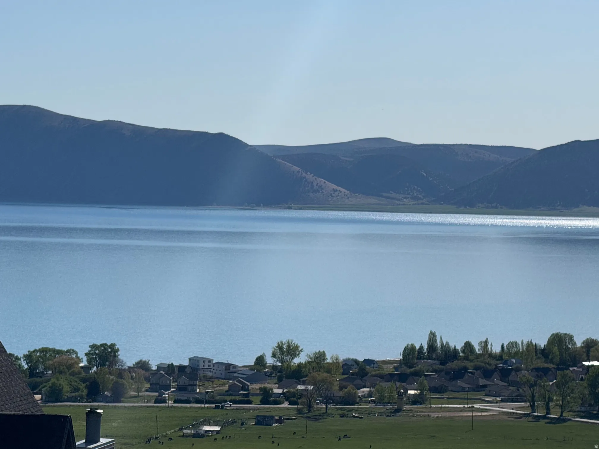Expansive water body framed by distant mountains and a foreground of green fields and scattered structures
