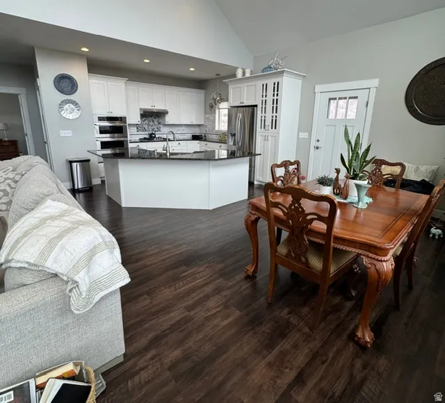 Dining area with dark wood-style floors, vaulted ceiling, and recessed lighting