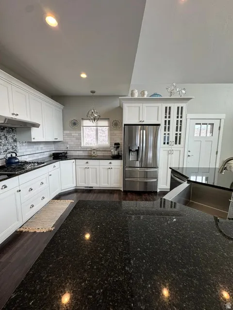 Kitchen featuring stainless steel appliances, white cabinetry, dark stone countertops, suspended lighting, and backsplash