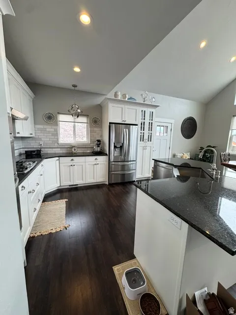 Kitchen featuring tasteful backsplash, stainless steel appliances, dark stone counters, white cabinets, and lofted ceiling