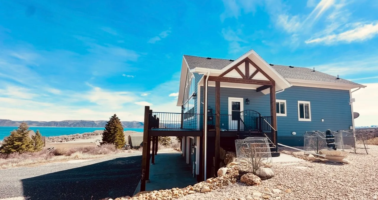 View of front of house with a deck with water view, a shingled roof, and a patio area