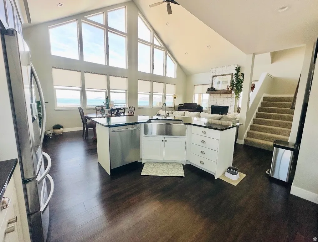 Kitchen featuring white cabinetry, a high ceiling, open floor plan, stainless steel appliances, and dark wood-type flooring