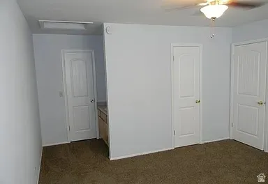 Unfurnished bedroom with dark colored carpet and a ceiling fan