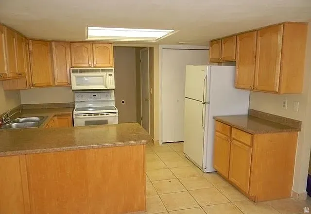 Kitchen featuring white appliances, a peninsula, light tile patterned flooring, and light countertops