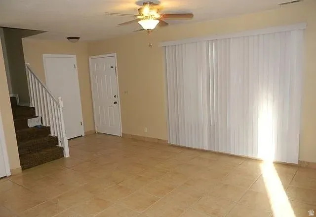 Unfurnished living room featuring stairway and a ceiling fan