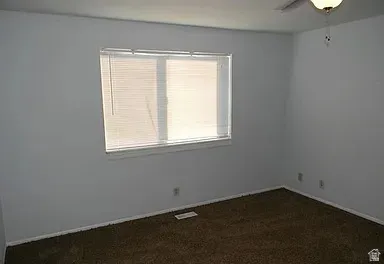 Unfurnished room with ceiling fan and dark colored carpet