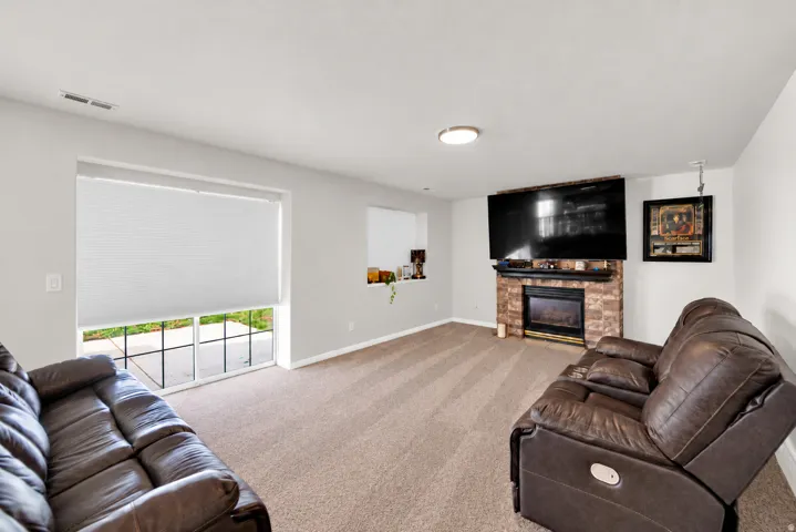 Carpeted living space featuring a stone-clad fireplace with a built-in media center, recessed lighting, and a large window with privacy blinds