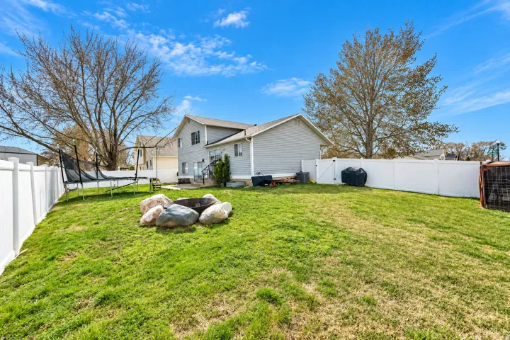 Expansive lawn with a built-in fire pit, surrounded by a white privacy fence