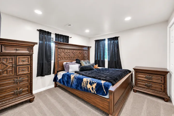 Recessed lighting illuminates the room, featuring two windows with horizontal blinds and a neutral carpeted floor