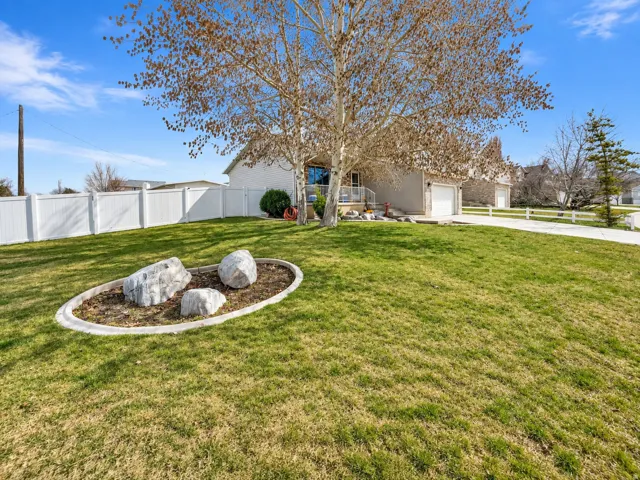 Expansive front yard featuring a manicured lawn, established tree, and decorative rock garden