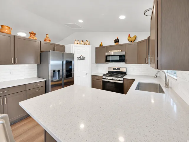 White subway tile backsplash, stainless steel appliances, wood-finish flooring, recessed lighting, and a large central island with light-toned countertops
