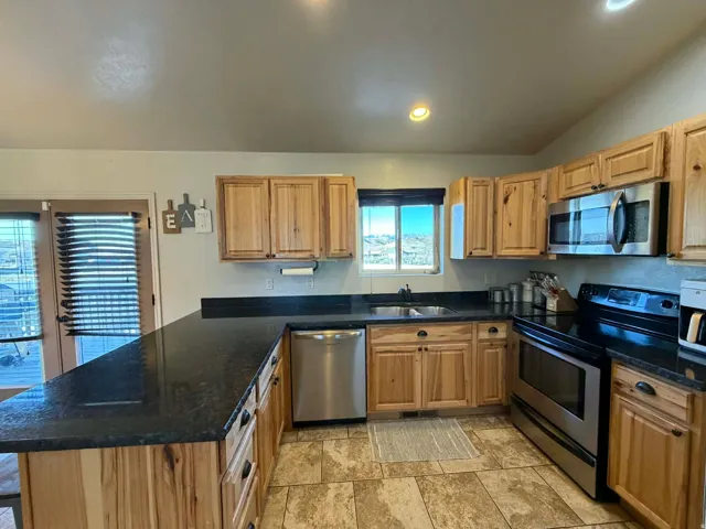 Kitchen with stainless steel appliances, a peninsula, dark stone counters, lofted ceiling, and recessed lighting